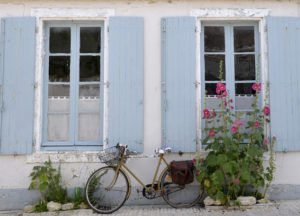 Vélo garé devant une maison bordée de roses trémières