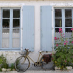 Vélo garé devant une maison bordée de roses trémières